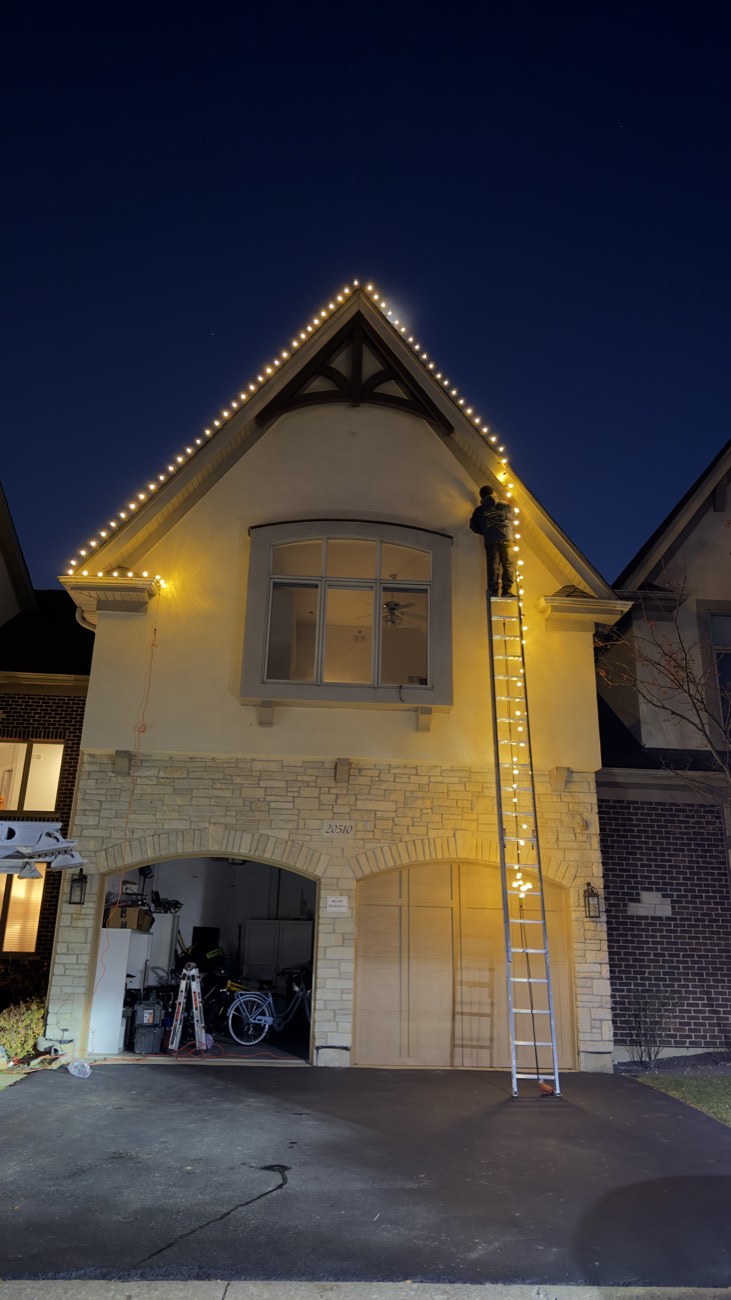 Technician installing permanent roofline lights on a two-story home