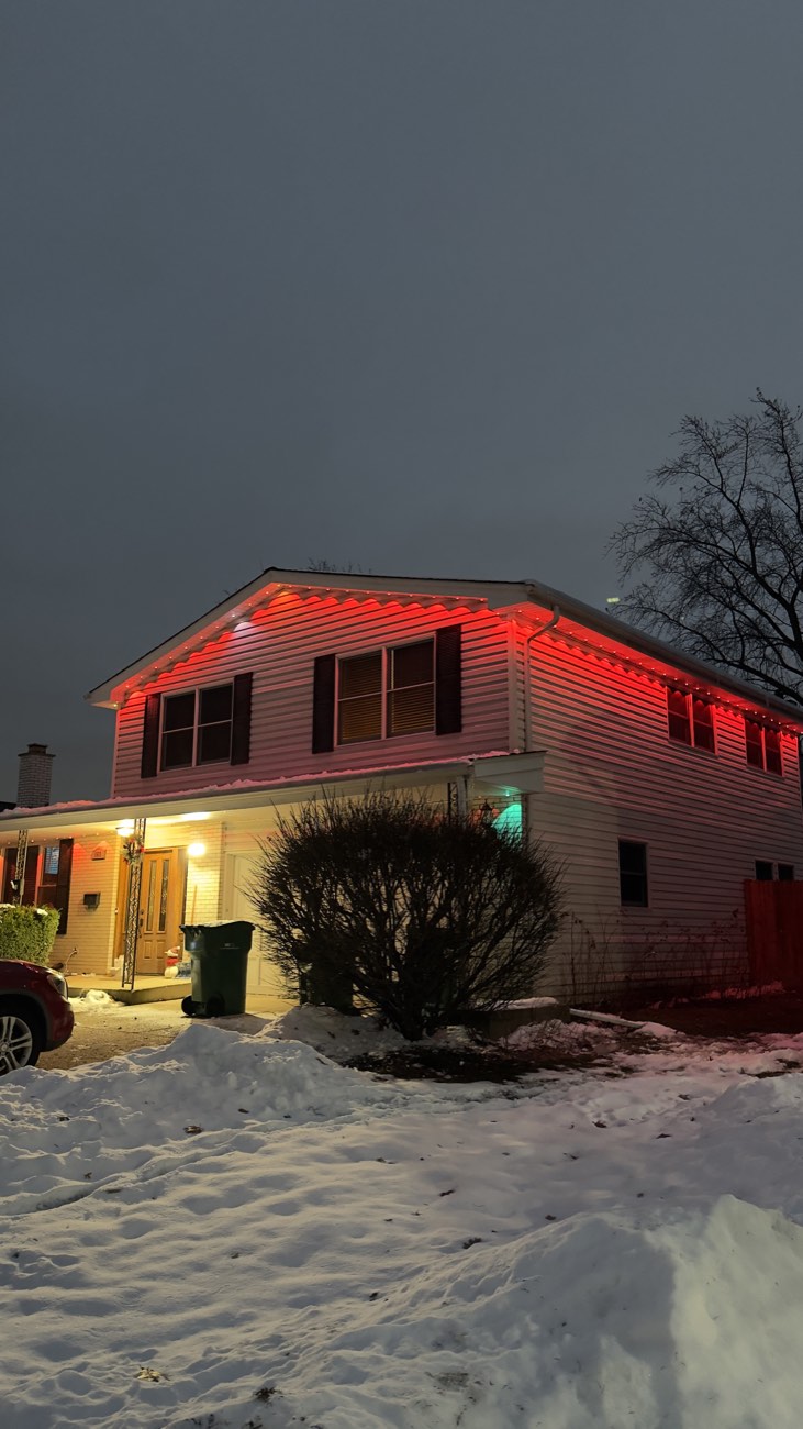 Red permanent holiday roofline lights on a home with snow