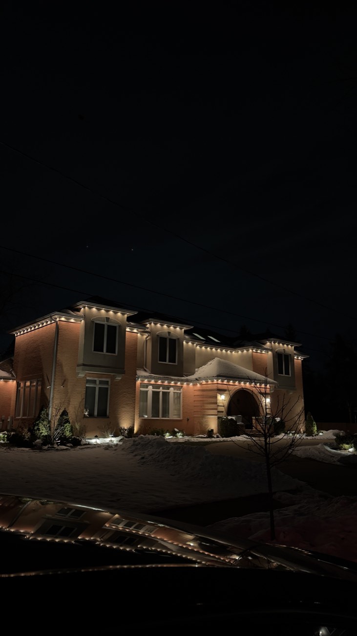 Warm white permanent roofline lighting outlining a large home in winter